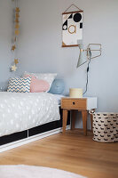 Scatter cushions on bed and bedside table below wall-mounted lamp in child's bedroom