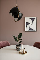 Houseplant and candle on table below lamp in dining room in earthy shades