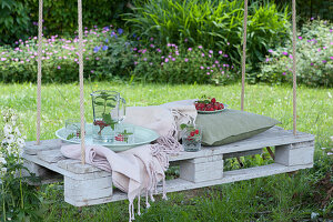 White pallet as a seat hung from a tree with ropes, jug with water, mint and raspberries