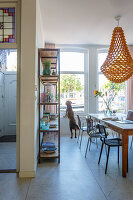 Pendant lamp above dining table and chairs, shelves and dog looking through window in background
