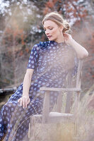 A blonde woman wearing a blue, polka-dot dress sitting in a garden