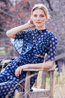 Blonde Frau in blauem, gepunktetem Kleid sitzt im Garten