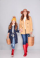 A mother and daughter wearing similar outfits (hats, jackets, jeans and red welly boots)