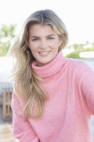 A young blonde woman wearing a pink turtle-neck jumper