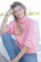 A young blonde woman wearing a pink turtle-neck jumper