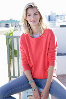 A young blonde woman wearing a coral-coloured turtle-neck jumper