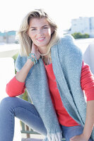 A young blonde woman wearing a coral-coloured jumper with a shawl over her shoulders