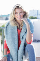 A young blonde woman wearing a coral-coloured jumper with a shawl over her shoulders