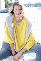 A young blonde woman wearing a yellow jumper and jeans