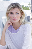 A young blonde woman wearing a purple t-shirt and a white jumper