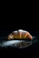 Ein Croissant mit Puderzucker vor schwarzem Hintergrund