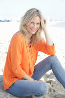 Blonde Frau in orangefarbener Tunikabluse und Jeans am Meer