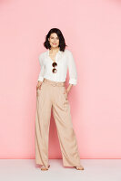 A brunette woman wearing wearing a white blouse and pink Marlene trousers