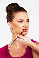 A brunette woman with her hair in a bun having her lipstick applied