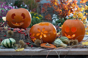 Halloween pumpkins with faces and floral decorations, decorative pumpkins, chestnuts, and a branch with rose hips