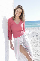 A long-haired woman on the beach wearing a pink top and a striped skirt