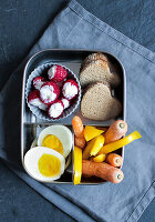 A breakfast box with heart-shaped bread, vegetables crudités, egg and stuffed raspberries
