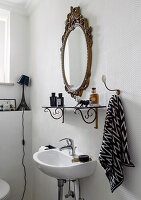 Antique mirror and shelf in white bathroom with textured wallpaper