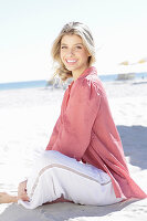 A young blonde woman wearing a pink top and white summer trousers