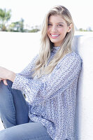 A young blonde woman wearing a blue-and-white patterned top and jeans