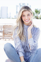 A young blonde woman wearing a blue-and-white patterned top and jeans