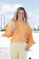 Junge blonde Frau in apricotfarbener Bluse und heller Hose