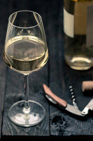 A glass of white wine with a bottle opener and wine bottle