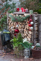 Brennholzlege weihnachtlich dekoriert mit Kiefernzweig, Christbaumkugeln und Tablett mit Kerzen