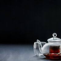 Schwarzer Tee in Glasteekanne vor schwarzem Hintergrund