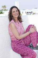 A long-haired woman wearing a pink sleeveless blouse and summer trousers