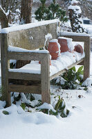 Holzbank und Tontöpfe im verschneiten Garten
