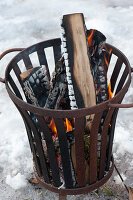 Feuerkorb mit brennenden Holzscheiten im Schnee