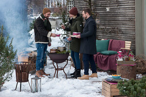 Friends standing comfortably around the barbecue, the woman pouring hot mulled wine