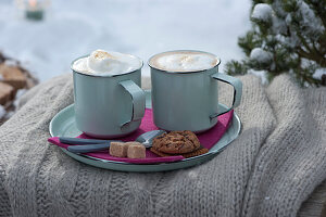 Tassen mit heißem Cappuccino auf Teller mit Zucker, Keks und Kaffeelöffeln