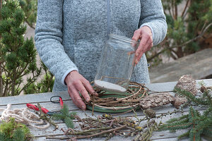 Windlicht mit Zweigen: Frau stellt Einmachglas in Kranz aus Clematisranken