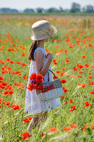 Girl holding basket in field of barley and poppies