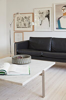 Floor lamp, black leather sofa, artwork above and coffee table with marble top in a bright living room