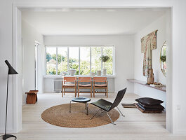 Black leather chair with footstool on round natural jute carpet, three chairs in front of the window in the white living room