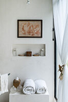 Rolled towel and glass vases on a cupboard, above is a wall niche with decorative objects and picture in bathroom