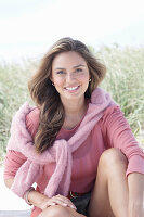 A young, long-haired woman wearing a pink blouse with a jumper over her shoulders