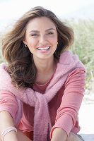 A young, long-haired woman wearing a pink blouse with a jumper over her shoulders