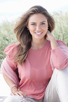 A young, long-haired woman wearing a pink blouse and light trousers