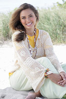 A young woman with long hair wearing a yellow t-shirt, a white crocheted jumper and trousers