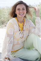 A young woman with long hair wearing a yellow t-shirt, a white crocheted jumper and trousers