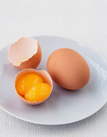 Ein ganzes braunes Ei und ein gufgeschlagenes  Ei mit doppeltem Eigelb