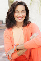 An older brunette woman wearing a salmon-coloured outfit