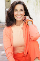 An older brunette woman wearing a salmon-coloured outfit