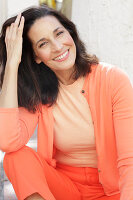 An older brunette woman wearing a salmon-coloured outfit