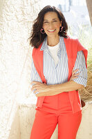 An older brunette woman wearing a blue-and-white striped shirt with a salmon-coloured jumper and trousers