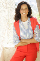 An older brunette woman wearing a blue-and-white striped shirt with a salmon-coloured jumper and trousers